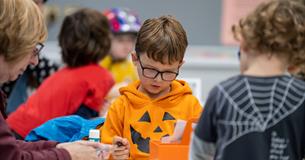 A young boy in an orange Halloween top takes part in a craft workshop