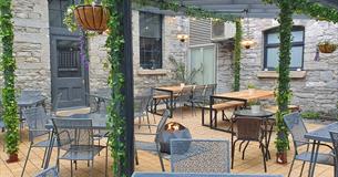 Outside courtyard area with tables and chairs, a fire pit and a plant covered pergola.