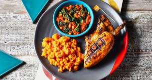 A grey plate with a portion of chicken, sweet potato mash and a green pot of beans and spinach.