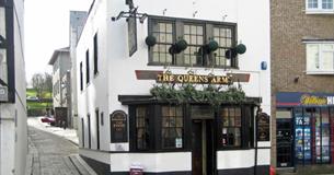 The white and black painted front of the Queens Arms with plant displays above the entrance.