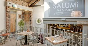 Inside Salumi, showing cream painted walls, tables and chairs, exposed brickwork and cream wrought iron railings separating seating areas.