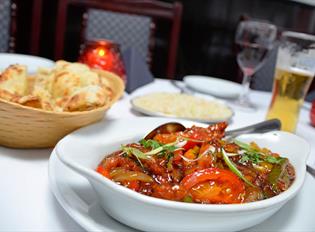 A table set for a meal with a bowl of curry, naan bread in a basket, a plate of rice, a drink and candles.