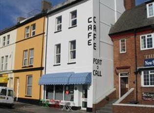 The outside of the Port O'Call Café showing brightly coloured awnings, outdoor tables and chairs and adjacent terraced properties.