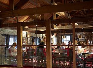 The inside of Miller & Carter with wooden beams, stone walls and diners sat at tables on black and red chairs.