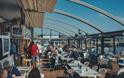 Inside the Boathouse Café with the roof retracted. Customers sitting at tables with a blue sky and views over Sutton Harbour.
