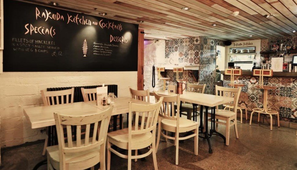 The inside of Bar Rakuda showing tables, chairs and a blackboard menu.