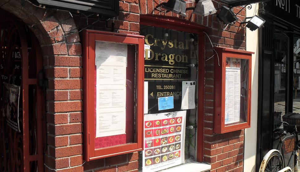 The red brick exterior of the restaurant with menus in red glass cases, pictures of various dishes and signage.