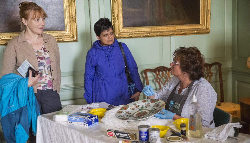 A conservator showing visitors how she cleans and cares for a ceramic dish