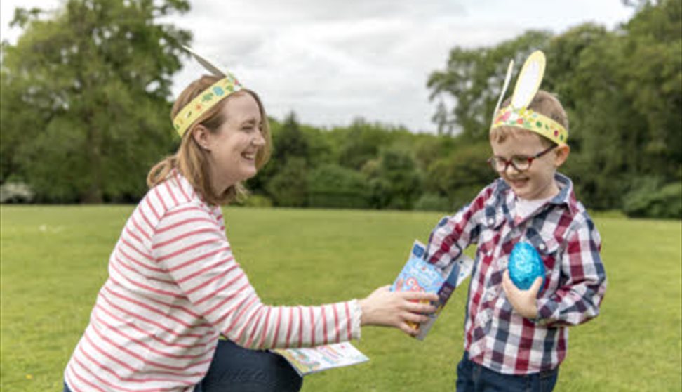 A woman and a young child in paper Easter bunny ears laughing and sharing a chocolate egg