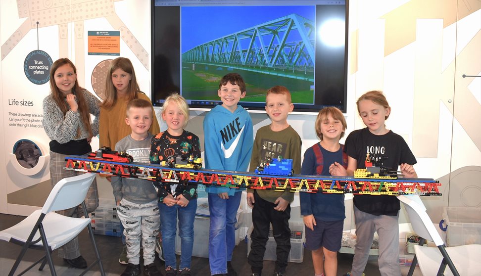 A line of children holding a long track made of lego.