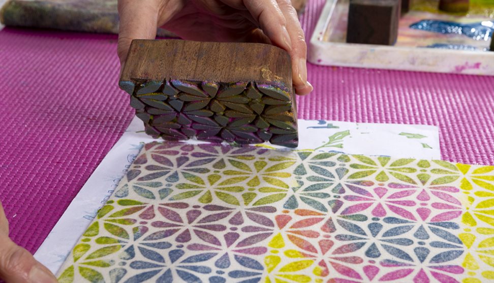 A colourful block-printed pattern on paper being created by hand