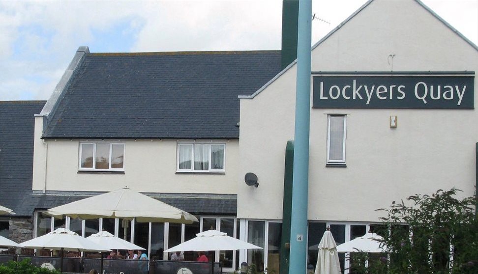 The outside of Lockyers Quay with outside seating and parasols in the foreground.