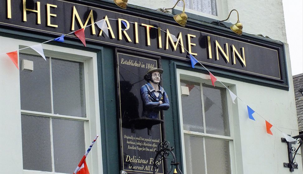 The pale green painted outside of The Maritime Inn with a painted figurehead affixed to the building and Union Jack bunting.