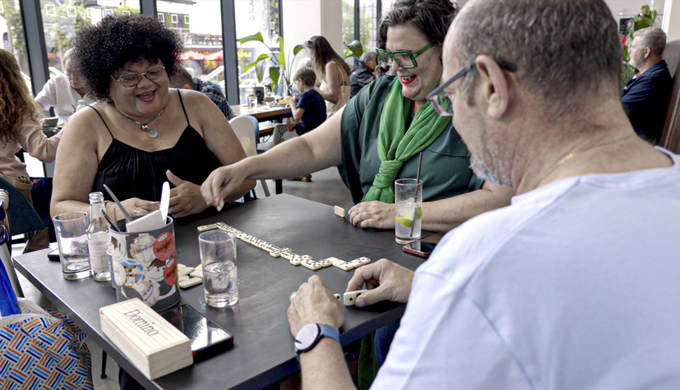 Three people sitting at a table playing a game of dominoes