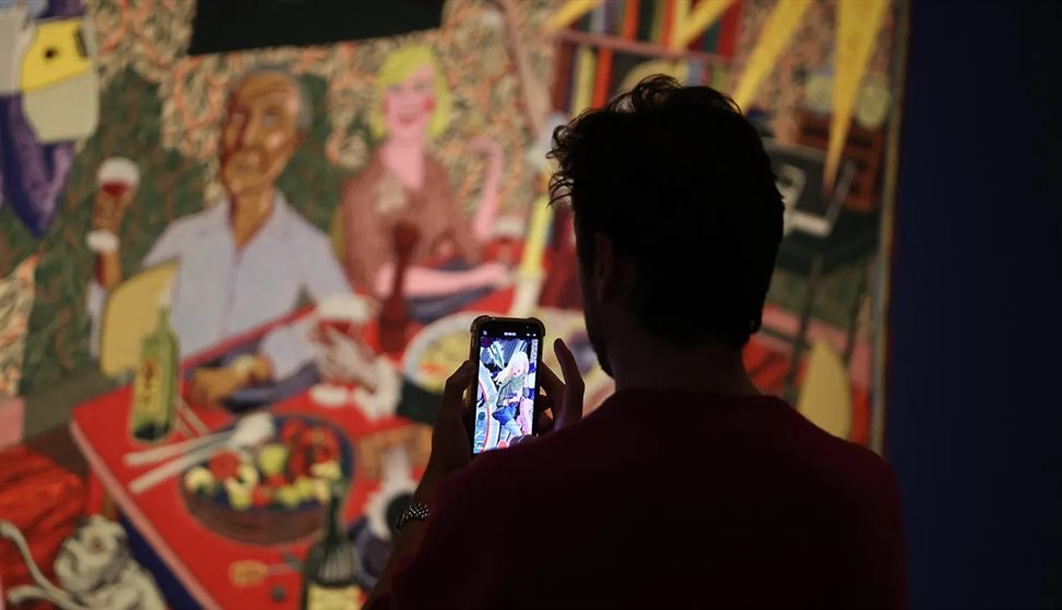 A person takes a photo of a Grayson Perry tapestry on their mobile phone