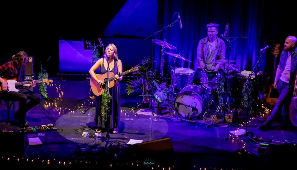 Photograph showing a woman standing on stage singing and playing the guitar