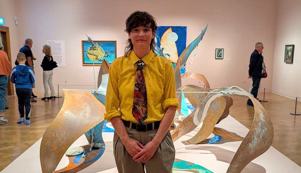 Photograph showing an artist in a gallery in front of their sculptural artwork