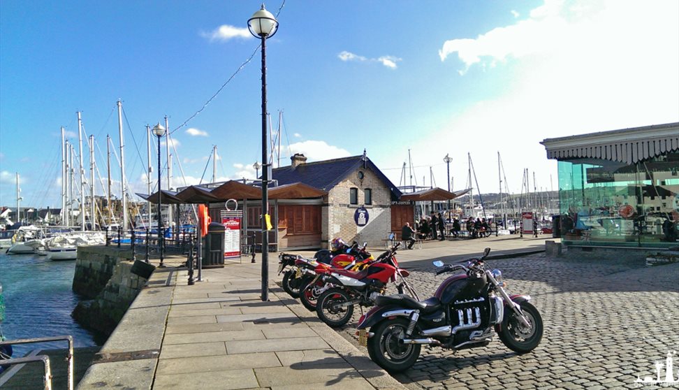 A distant shot of Cap'n Jaspers at the end of the quay with yachts in the background and motorbikes parked outside.