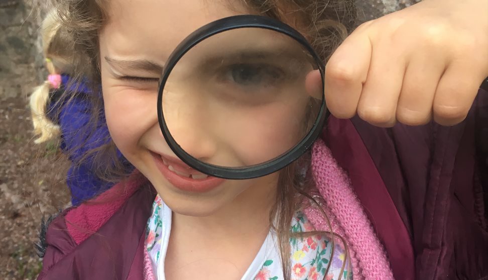 Child looks at camera through magnifying glass