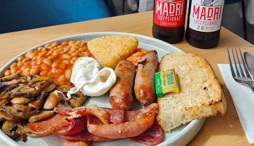 A full English breakfast on a plate with two bottles of Madri beer behind it