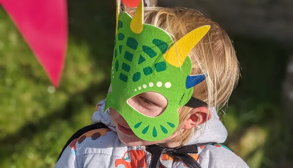 A child wearing a green dragon mask
