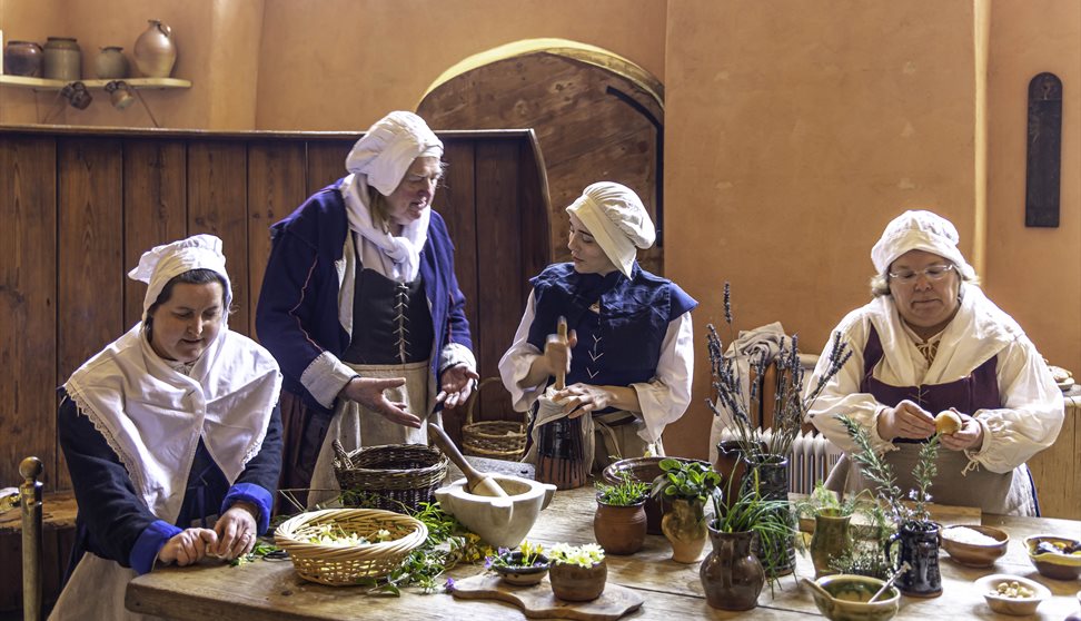 A group of people dressed in Tudor costume cooking in a historic kitchen
