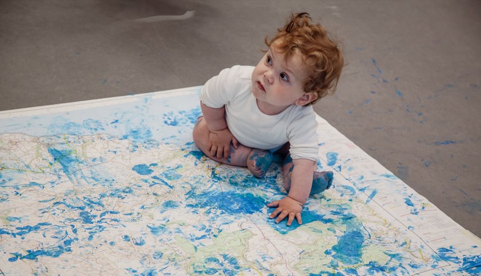 Photograph of a child sitting on a map which has blue paint on it