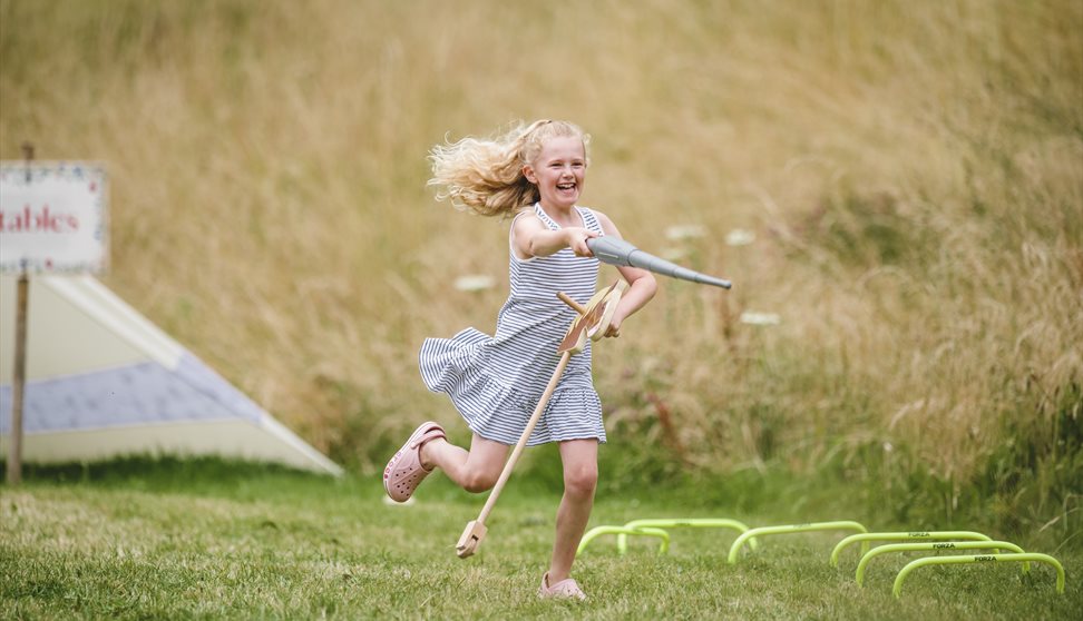 A girl on a hobby horse with a toy lance pretending to joust