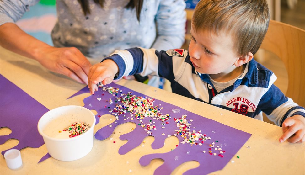 A toddler playing with arts and crafts at the aquarium as their parents looks over them