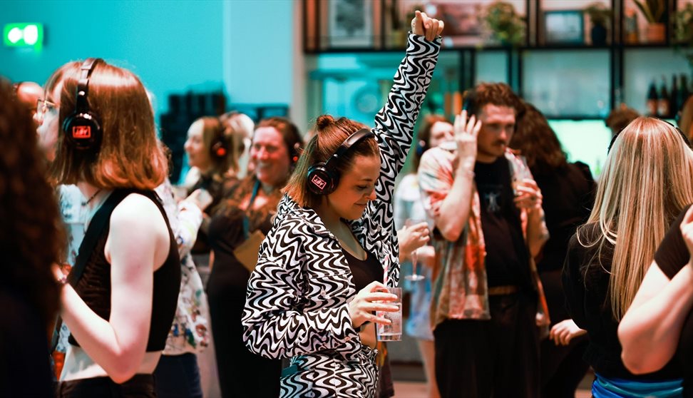 A girl dressed in black and white and holding a drink dances at a silent disco