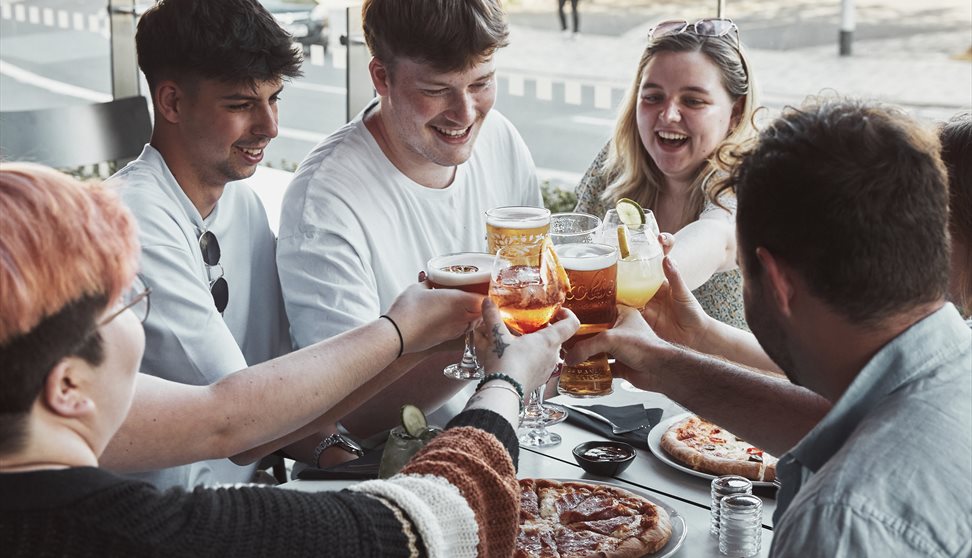 Crowd around a pizza with drinks