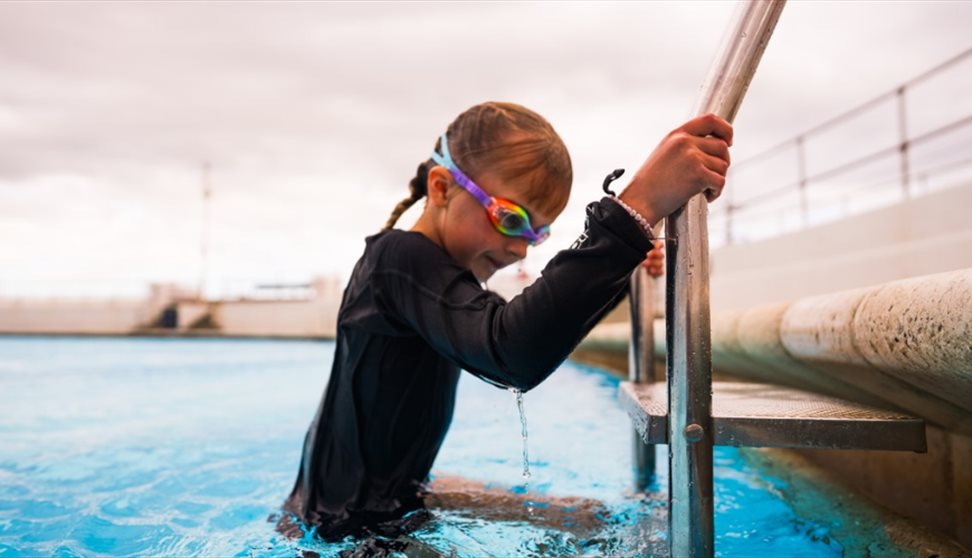 A child climbing up a ladder out of a swimming pool at Tinside Lido