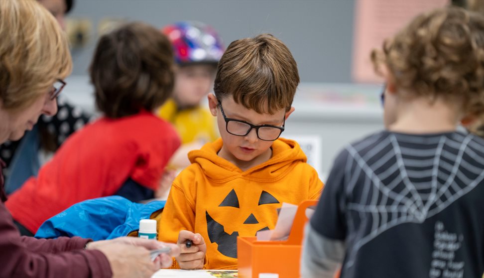 A young boy in an orange Halloween top takes part in a craft workshop