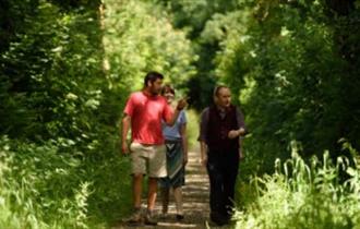 A National Trust Ranger giving a tour to visitors in a green woodland setting.