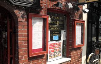 The red brick exterior of the restaurant with menus in red glass cases, pictures of various dishes and signage.