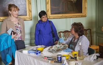 A conservator showing visitors how she cleans and cares for a ceramic dish