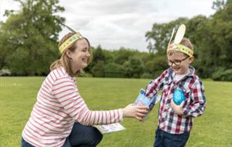 A woman and a young child in paper Easter bunny ears laughing and sharing a chocolate egg