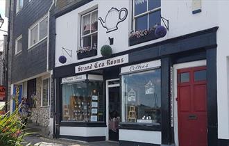 Shop front of The Strand Tea Rooms, painted black and white and with a large painted teapot above the sign.