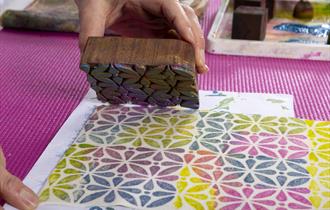 A colourful block-printed pattern on paper being created by hand