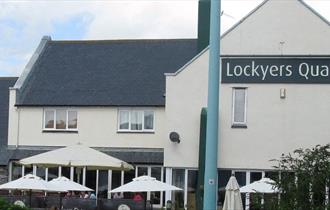 The outside of Lockyers Quay with outside seating and parasols in the foreground.