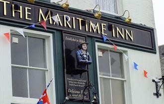 The pale green painted outside of The Maritime Inn with a painted figurehead affixed to the building and Union Jack bunting.