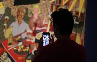 A person takes a photo of a Grayson Perry tapestry on their mobile phone