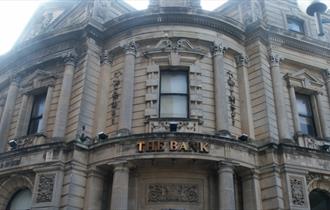 The stone exterior of The Bank with stone pillars and arches and a metal sign saying The Bank.