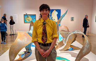 Photograph showing an artist in a gallery in front of their sculptural artwork