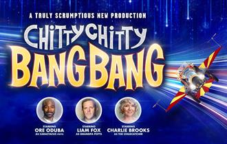 Blue backdrop with flying chitty car and cast members, Ore Oduba, Liam Fox and Charlie Brooks.