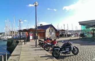 A distant shot of Cap'n Jaspers at the end of the quay with yachts in the background and motorbikes parked outside.