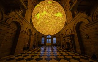 A glowing sun-like sphere hangs in the centre of an ornate hall with arched doorways, high ceilings, and a black-and-white checkered floor.