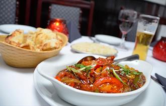 A table set for a meal with a bowl of curry, naan bread in a basket, a plate of rice, a drink and candles.