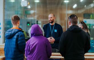 A man addresses a group of attentive individuals, standing at the forefront and sharing his insights.
