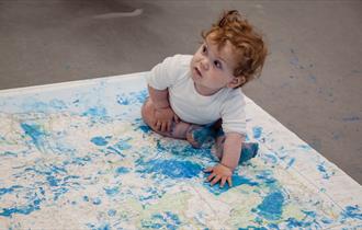 Photograph of a child sitting on a map which has blue paint on it